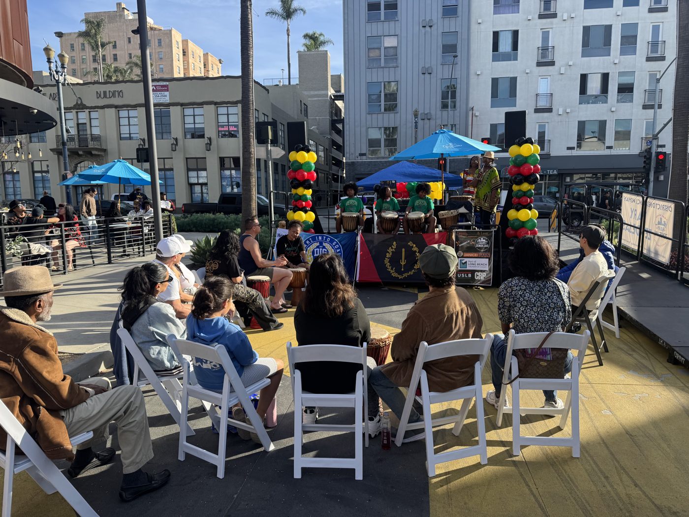 Community members seated on the DTLB Promenade watching youth drummers perform