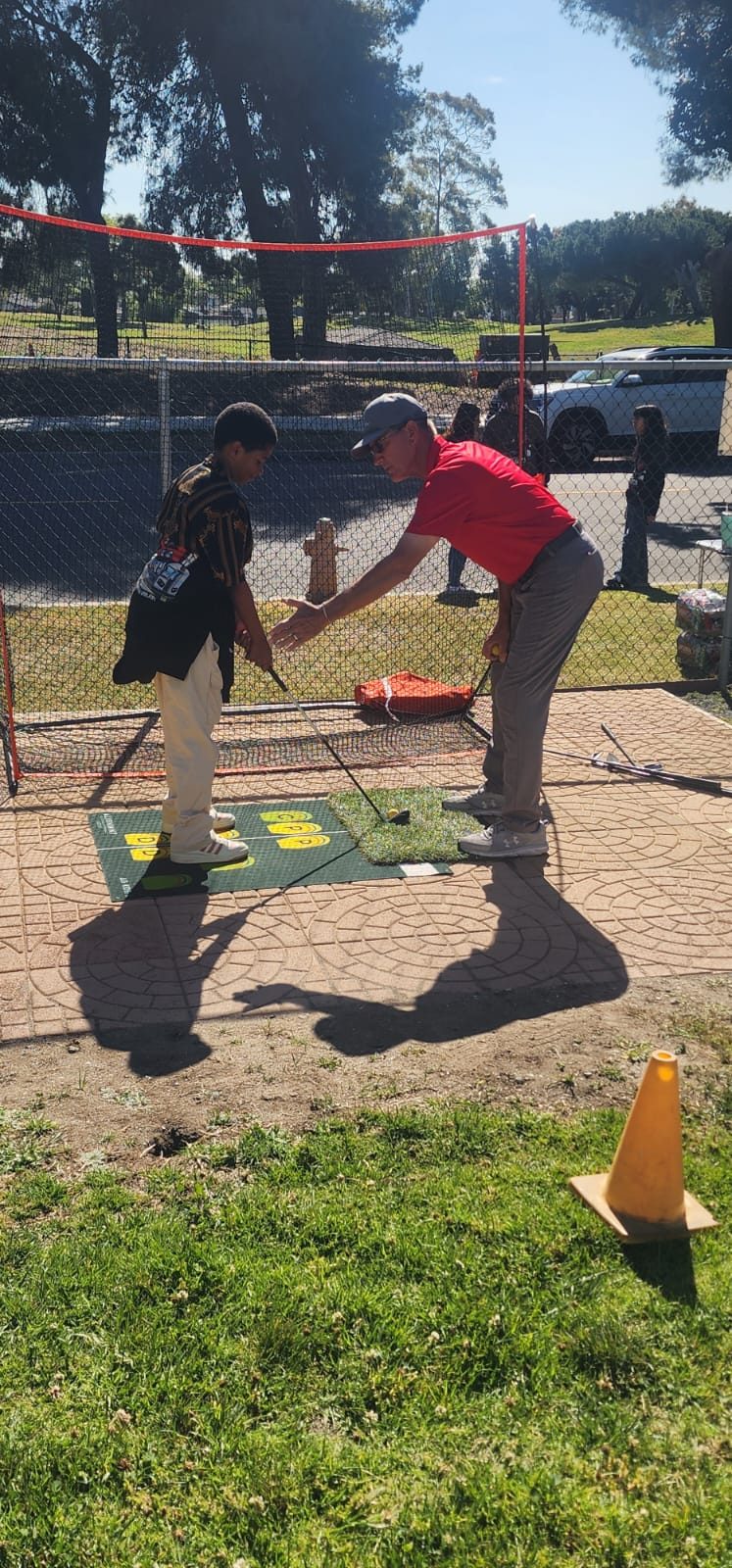 A TGA Golf Academy coach guiding a student through his swing at the practice net.
