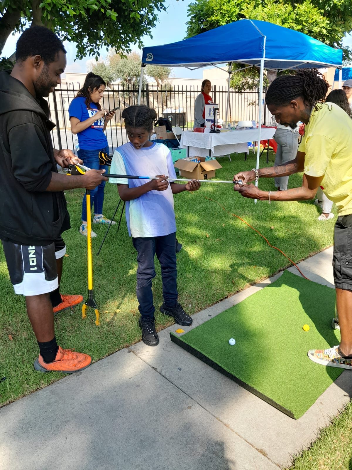 A young participant being fitted with a golf club by two coaches.