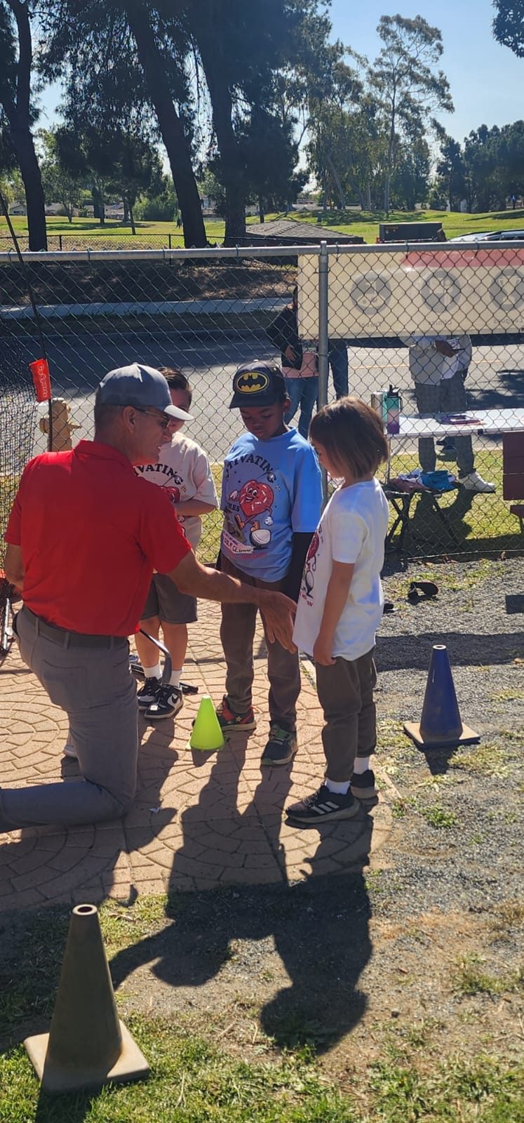 A coach kneeling to explain a drill to three young golfers.
