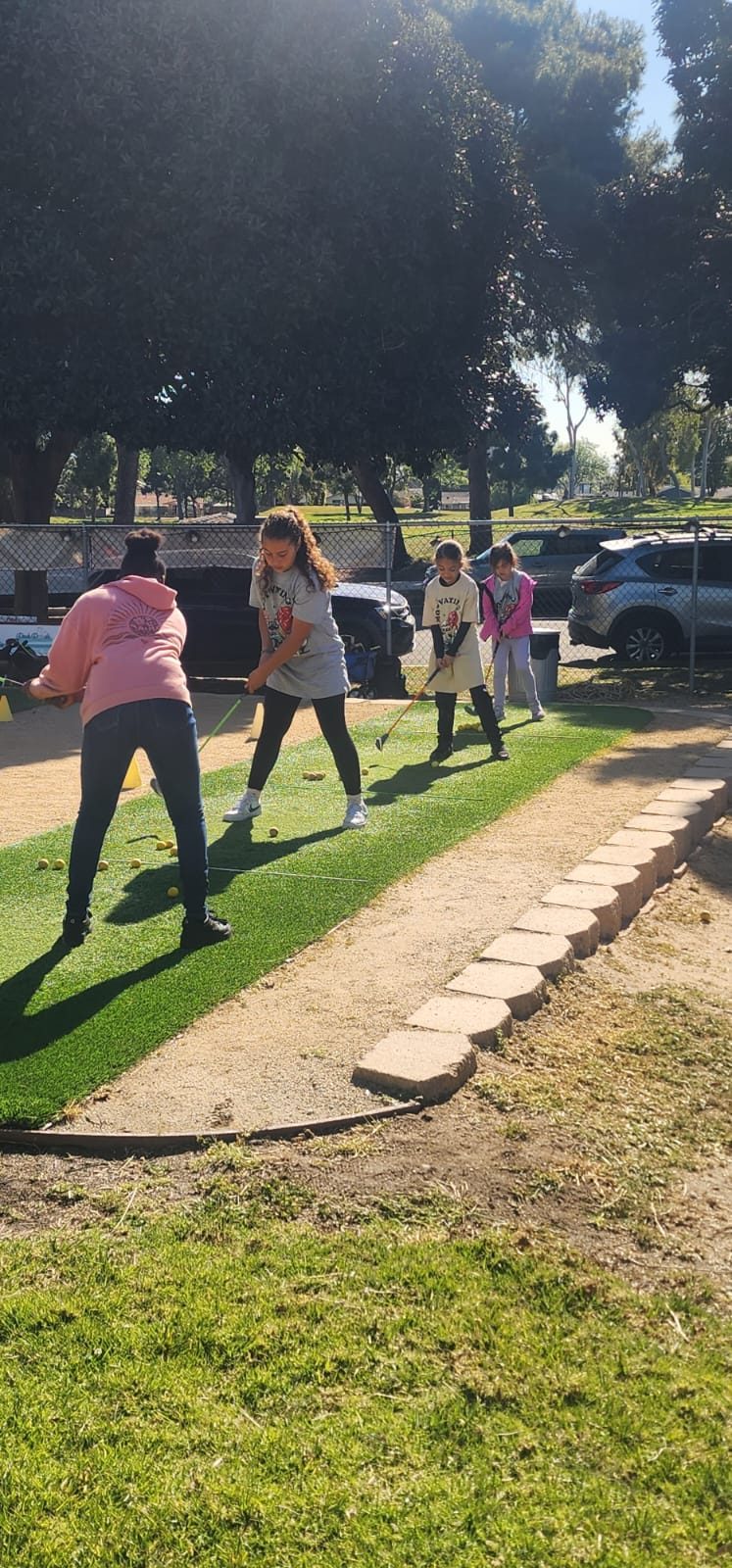 Four students lined up on the practice turf working on their swings.