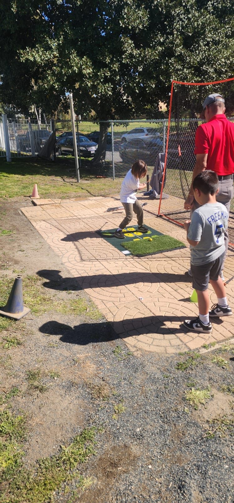A student taking a full swing into the practice net while a coach and another student watch.