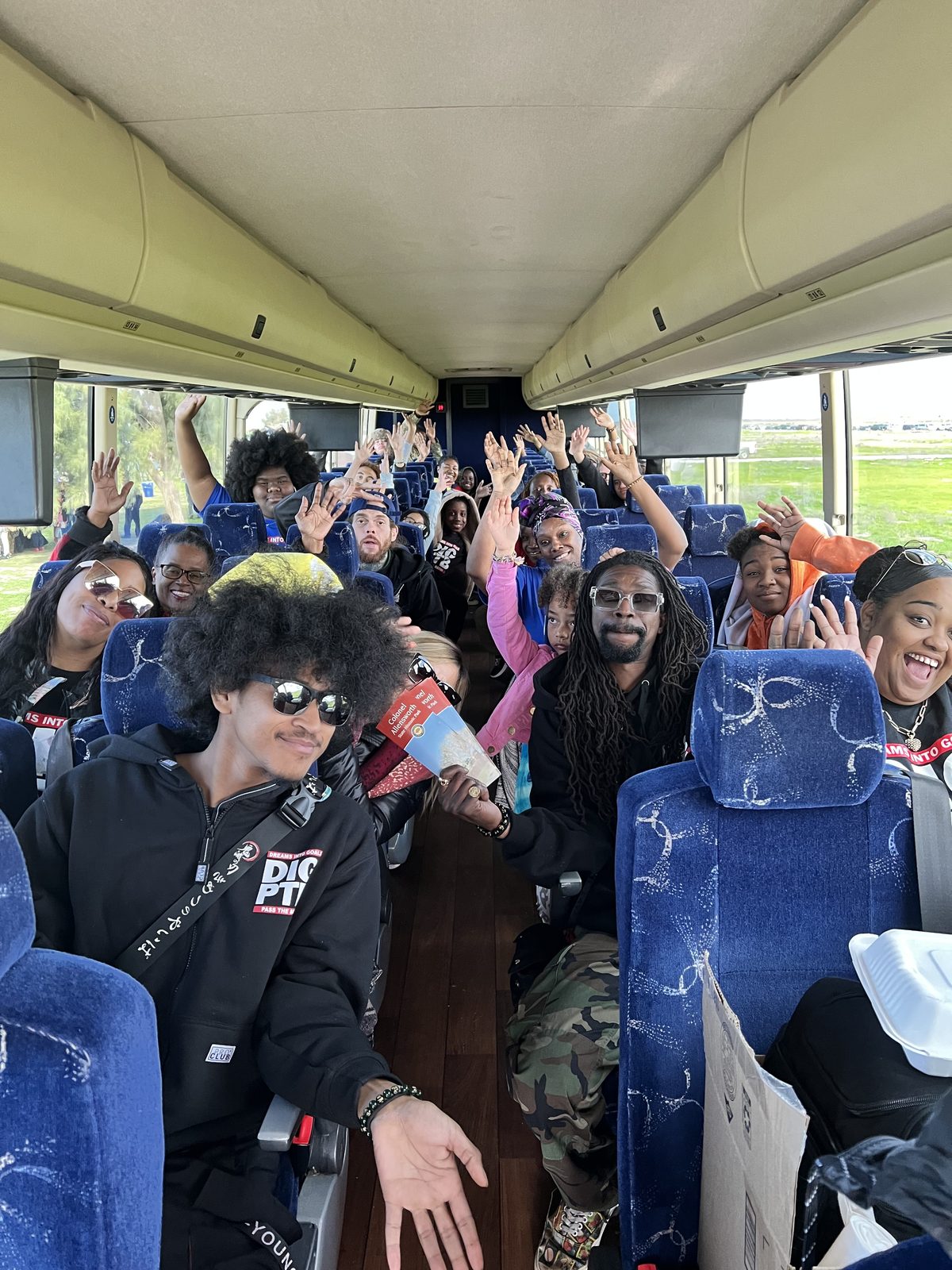 DIG LIFE students, families, and chaperones with their hands up on the bus to Allensworth.