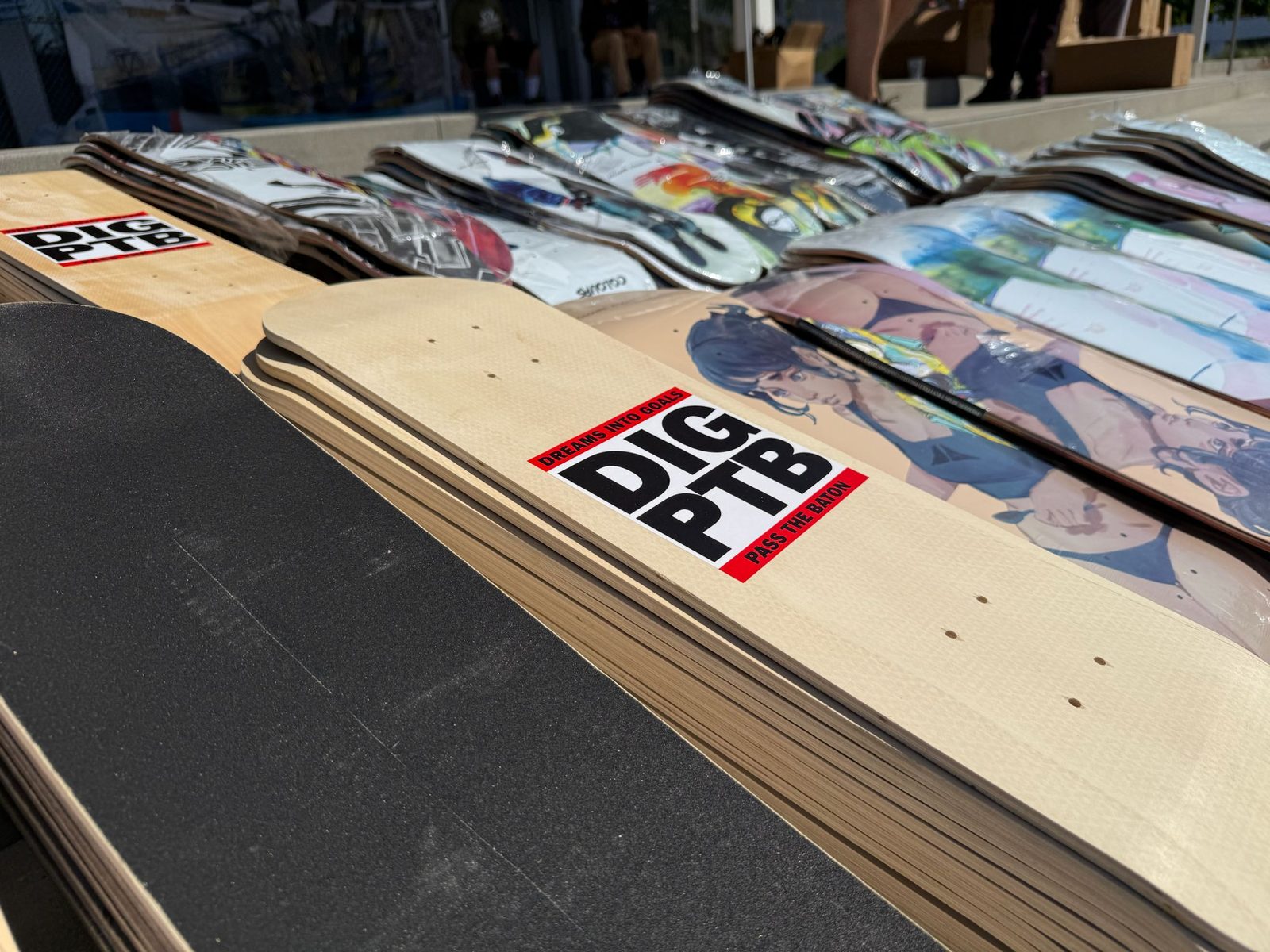 Rows of skateboard decks stickered with the DIG PTB 'Pass The Baton' logo, ready to be given away.