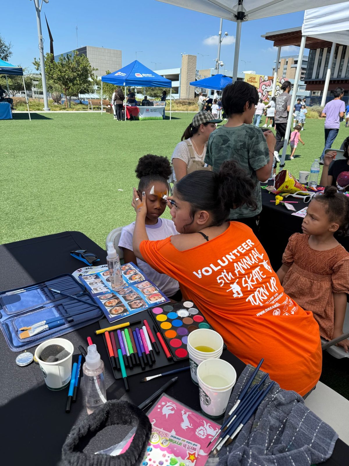 A volunteer in a 5th Annual Skate Turn Up shirt painting a child's face.