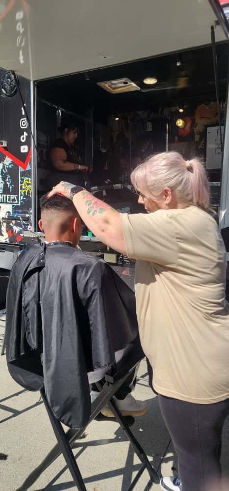 A barber giving a free haircut inside a mobile barbershop trailer.