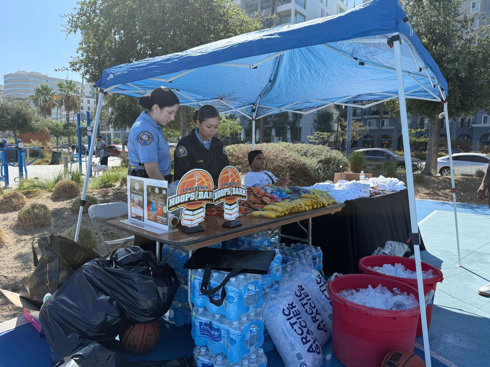 Long Beach Police Explorers staffing the Hoops After Dark resource table with water, snacks, and giveaway shirts.